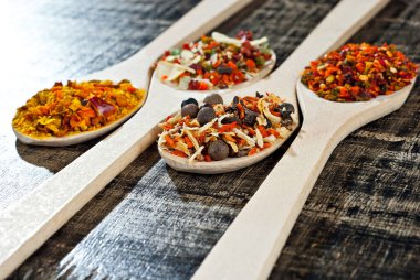 Tahta kaşıkta çeşitli baharatların karışımı. Eski püskü bir tahtada baharatlar ve baharatlar. Yakın çekim yığını üzerinde karıştır.