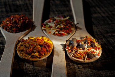 Tahta kaşıkta çeşitli baharatların karışımı. Eski püskü bir tahtada baharatlar ve baharatlar. Yakın çekim bir yığın karıştırın. Sanatsal bir efekt olarak dramatik ışık karşıtlığı.