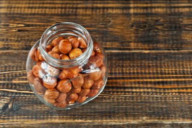 Şeffaf cam kavanozda fındık kabuğu soyulmuş. Eski püskü bir tahtada fındıklar. Kavanozu kahverengi tahta bir masaya yakın tut.. 