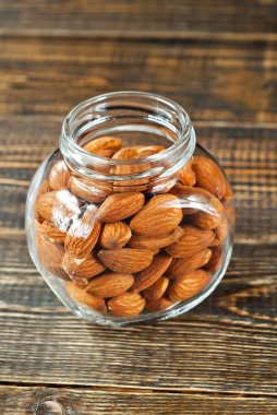 Cam şeffaf kavanozdaki bademler. Eski püskü bir tahtada fındıklar. Kavanozu kahverengi tahta bir masaya yakın tut.. 