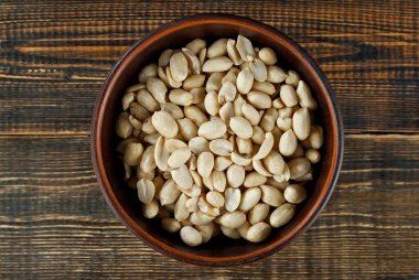 Eski püskü bir tahtanın üzerindeki kil kasede yer fıstığı. Kahverengi ahşap masada fındıklar.