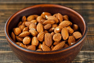 Eski püskü bir tahtanın üzerindeki kil kasede badem. Kahverengi ahşap masada fındıklar.