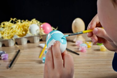Çocuk bir Paskalya yumurtası boyuyor. Mavi boyalı beyaz yumurta. Yaklaş..