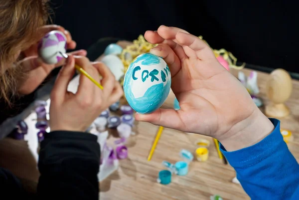 Mother and son paint Easter eggs. Multi Colored Easter eggs on a wooden table background. Traditional family entertainment before the holiday. An egg with the inscription \