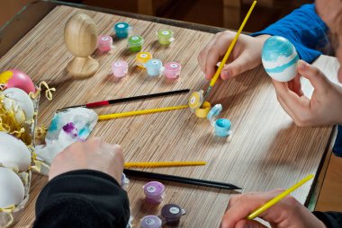Anne ve oğlu Paskalya yumurtalarını boyar. Ahşap masa arkasında çok renkli Paskalya yumurtaları. Bayramdan önce geleneksel aile eğlencesi.