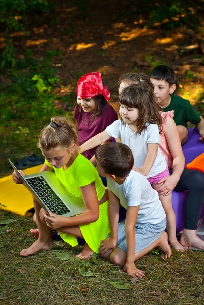 Children play in nature with a laptop. Boys and girls are resting in a tent camp. Children sit on a purple inflatable sofa in summer.