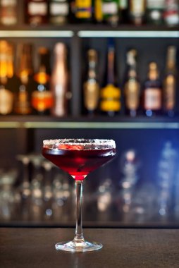 Bar tezgahında kırmızı kokteyl. Martini, cin, rom, tekila ve alkollü şişelerin arkasında meyve ile birlikte iç. Ahşap bir tahtanın üzerinde içki bardağı.