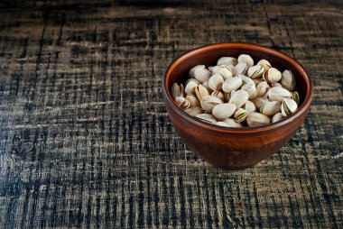 Döküntü bir tahta üzerinde kil bir kasede fıstıklar. Siyah bir masada kabuklu fındıklar. Fındık yakınındaki metin için boşluk ve boş alanı kopyala.