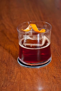 Bar tezgahında sarı kokteyl. Barın arka planında viski, rom ya da brendi. Ahşap bir tahtanın üzerinde içki bardağı.