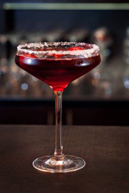 Bar tezgahında kırmızı kokteyl. Martini, cin, rom, tekila ve alkollü şişelerin arkasında meyve ile birlikte iç. Ahşap bir tahtanın üzerinde içki bardağı.