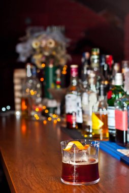 Bar tezgahında sarı kokteyl. Alkollü şişelerin arka planında viski, rom veya brendi. Ahşap bir tahtanın üzerinde içki bardağı.