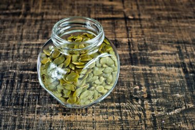 Ahşap bir masada cam kavanozdaki kabak çekirdekleri soyulmuş. Siyah, pejmürde bir tahtanın üzerindeki tohumlar. Çekirdeklere yakın metin için boşluk ve boşluk kopyala.