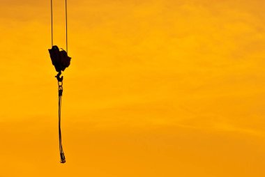 Gün batımının arka planında bir vinç silueti. Turuncu arka planda halatlar ve kancalar.