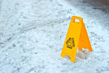 Sarı tehlike işareti. Kaygan bir kaldırımın sembolü. Farklı dillerde yazıt dikkati. İlkbaharda kaldırım taşlarının yanındaki tabakta..