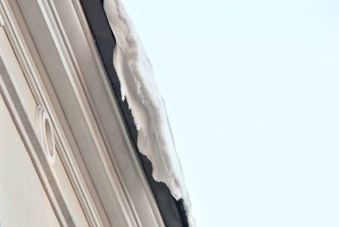 Evin çatısında buz saçakları asılı. Tehlike ve kaygan kaldırımlar kavramı. Şehirde ilkbaharın başlangıcı. Şeffaf kuğu buz saçakları kapanıyor.