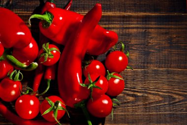 Biberler, dolmalık biberler ve kahverengi tahta üzerinde kırmızı domatesler. Sanatsal bir efekt olarak dramatik bir ışık. Biber yakınındaki metin için boşluk ve boş alanı kopyala.