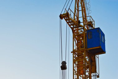 Gün batımının arka planında bir vinç silueti. İpler ve kancalar mavi arkaplanda.