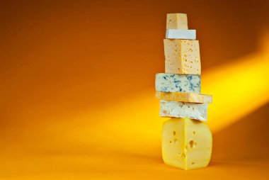 Turuncu arka planda sarı peynir. Farklı peynir yığınları var. Peynir kulesi. Peynir yakınındaki metin için boşluk ve boş alanı kopyala.