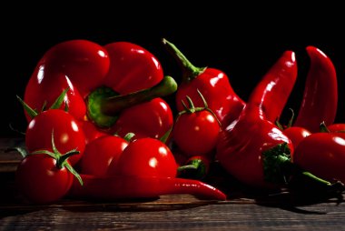 Biberler, dolmalık biberler ve kahverengi tahta üzerinde kırmızı domatesler. Sanatsal bir efekt olarak dramatik ışık karşıtlığı.