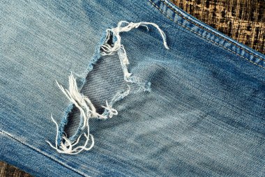 Siyah tahta arka planda mavi yırtık kot pantolon. Pantolondaki delik kapanır. Giysiler ve yoksulluk kavramı.