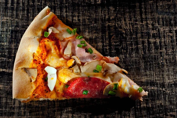 Tahta üzerinde üçgen pizza dilimi. Siyah bir masada pizza, yakın plan. Yemek yakınındaki metin için boşluk ve boş alanı kopyala.