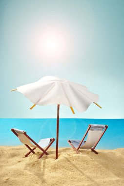 Kumsaldaki şemsiyeler ve kumdaki güneşlikler. Stilize karton plaj. Arka planda kokteyller için kağıt şemsiyeler. Dinlenme, deniz ve tatil kavramı. Yapay tahta şezlonglar..