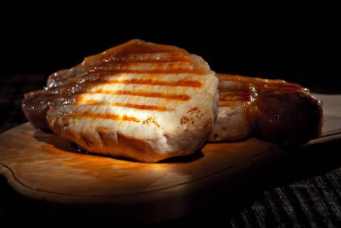 Siyah arka planda ahşap bir tahtada biftek. Eski püskü bir masada kızarmış et. Sanatsal bir efekt olarak dramatik ışık karşıtlığı.