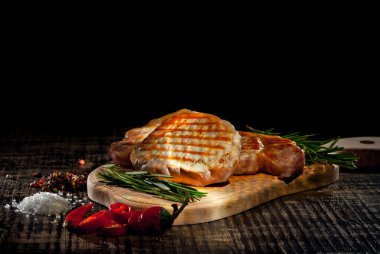 Siyah arka planda ahşap bir tahtada biftek. Eski püskü bir masada kızarmış et. Biberiye biberi ve bifteğin yanında tuz. Sanatsal bir efekt olarak dramatik ışık karşıtlığı.