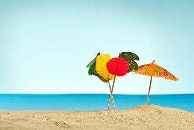 Kumsaldaki şemsiyeler. Stilize karton plaj. Arka planda kokteyller için kağıt şemsiyeler. Dinlenme, deniz ve tatil kavramı.