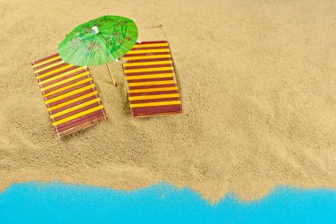 Kumsaldaki şemsiyeler ve kumdaki güneşlikler. Stilize karton plaj. Arka planda kokteyller için kağıt şemsiyeler. Dinlenme, deniz ve tatil kavramı. Yapay tahta şezlonglar..