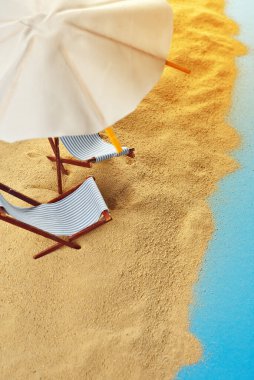 Kumsaldaki şemsiyeler ve kumdaki güneşlikler. Stilize karton plaj. Arka planda kokteyller için kağıt şemsiyeler. Dinlenme, deniz ve tatil kavramı. Yapay tahta şezlonglar..