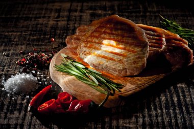 Siyah arka planda ahşap bir tahtada biftek. Eski püskü bir masada kızarmış et. Biberiye biberi ve bifteğin yanında tuz. Sanatsal bir efekt olarak dramatik ışık karşıtlığı.