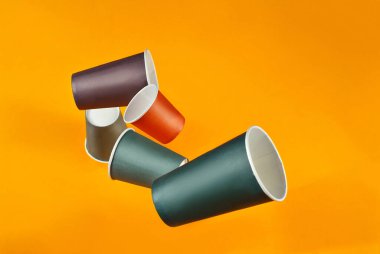 Tek kullanımlık kağıt bardaklar turuncu arka plana düşer. Farklı boyutlarda ve renkte camlar kapanıyor. Tabakların yanındaki metin için boşluk ve boşluk kopyala.