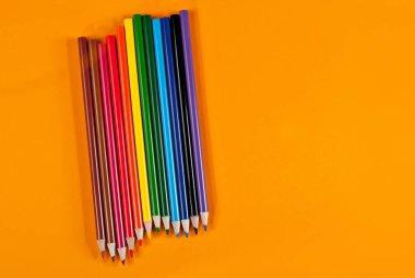 Turuncu arka planda çok renkli kalemler. Sarı arkaplan üzerindeki metin için boşluk ve boşluk kopyala.