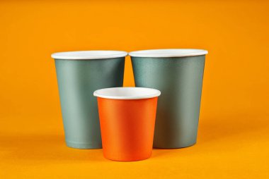 Turuncu arka planda tek kullanımlık kağıt bardaklar. Farklı boyutlarda ve renkte camlar kapanıyor. Farklı içecekler için parti aletleri.