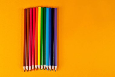 Turuncu arka planda çok renkli kalemler. Sarı arkaplan üzerindeki metin için boşluk ve boşluk kopyala.