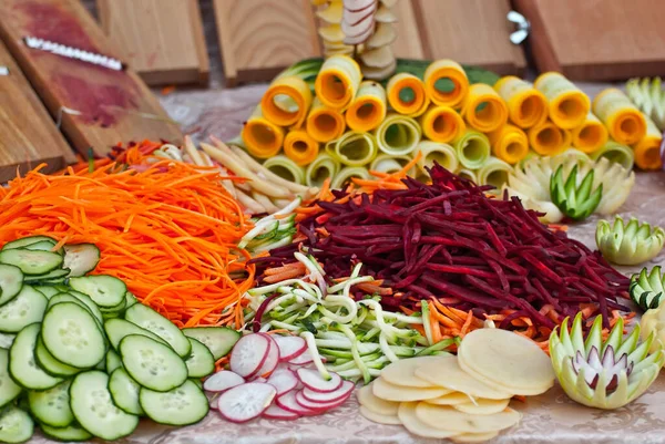 Masada bir sürü kesilmiş sebze var. Meyveleri öğütmek için mutfak aletleri gösterisi. Festivalde yararlı yemekler..