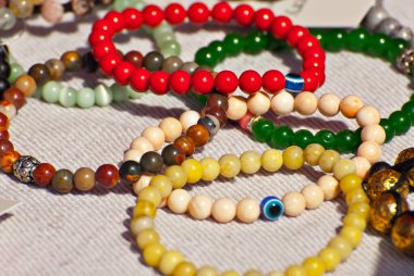 Masanın üzerinde renkli taşlardan bir kolye var. Doğal değerli minerallerden yapılmış birçok farklı mücevher ve boncuk. Boncuklu mücevherler fuarda satılıyor..