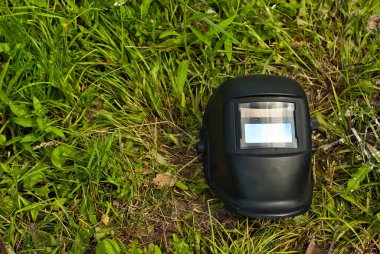 Kaynak yapmak için koruyucu kask. Yeşil çimlerin üzerindeki kaynak makinesinin maskesi.