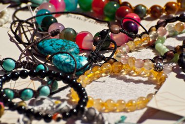 Masanın üzerinde renkli taşlardan bir kolye var. Doğal değerli minerallerden yapılmış birçok farklı mücevher ve boncuk. Boncuklu mücevherler fuarda satılıyor..