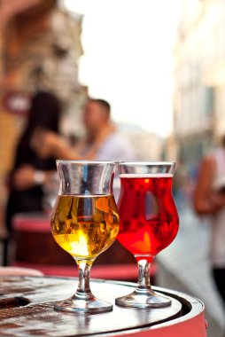 Bir kadeh kırmızı ve beyaz şarap. Alkolik likör, şehrin arka planında tahta bir fıçıda. Arka planda öpüşen bulanık çift..