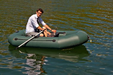 Şişme teknede beyaz gömlekli bir adam. Göl kenarında dizüstü bilgisayarı olan bir iş adamı. Uzaktan çalışma, boş zaman ve serbest çalışma kavramı..