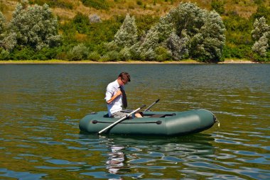 Şişme teknede beyaz gömlekli bir adam. Göl kenarında dizüstü bilgisayarı olan bir iş adamı. Uzaktan çalışma, boş zaman ve serbest çalışma kavramı..