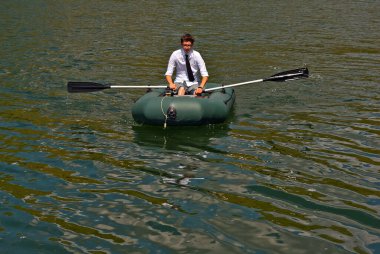 Şişme teknede beyaz gömlekli bir adam. Göl kenarında dizüstü bilgisayarı olan bir iş adamı. Uzaktan çalışma, boş zaman ve serbest çalışma kavramı..