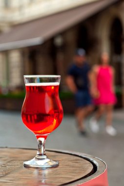 Bir kadeh kırmızı şarap yakın çekim. Alkolik likör, şehrin arka planında tahta bir fıçıda. Arka planda bulanık insanlar.