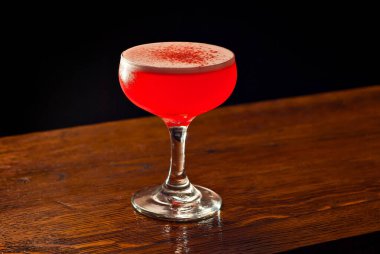 Bar tezgahında kırmızı kokteyl. Martini, cin, rom, tekila ve alkollü şişelerin arkasında meyve ile birlikte iç. Ahşap bir tahtanın üzerinde içki bardağı.