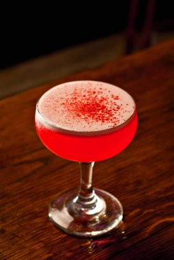 Bar tezgahında kırmızı kokteyl. Martini, cin, rom, tekila ve alkollü şişelerin arkasında meyve ile birlikte iç. Ahşap bir tahtanın üzerinde içki bardağı.