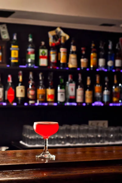 バーカウンターで赤いカクテル アルコールとボトルの背景にマティーニ ラム酒 テキーラとフルーツを飲みます 板に酒を盛ったガラス — ストック写真