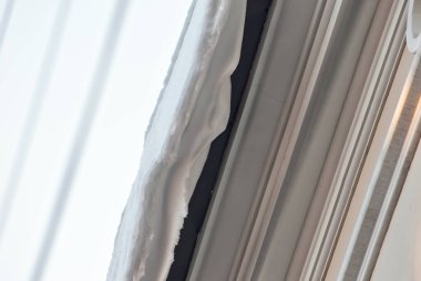 Evin çatısında buz saçakları asılı. Tehlike ve kaygan kaldırımlar kavramı. Şehirde ilkbaharın başlangıcı. Şeffaf kuğu buz saçakları kapanıyor.