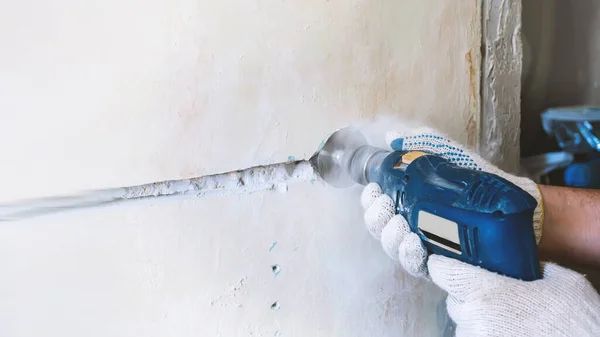 worker drills a hole for an electrical outlet in a concrete brick wall. repair of electrical wiring. construction worker with a pneumatic hammer drill drill with a diamond crown makes a hole in the wall for an electric cable, outlet, switch. Copy spa